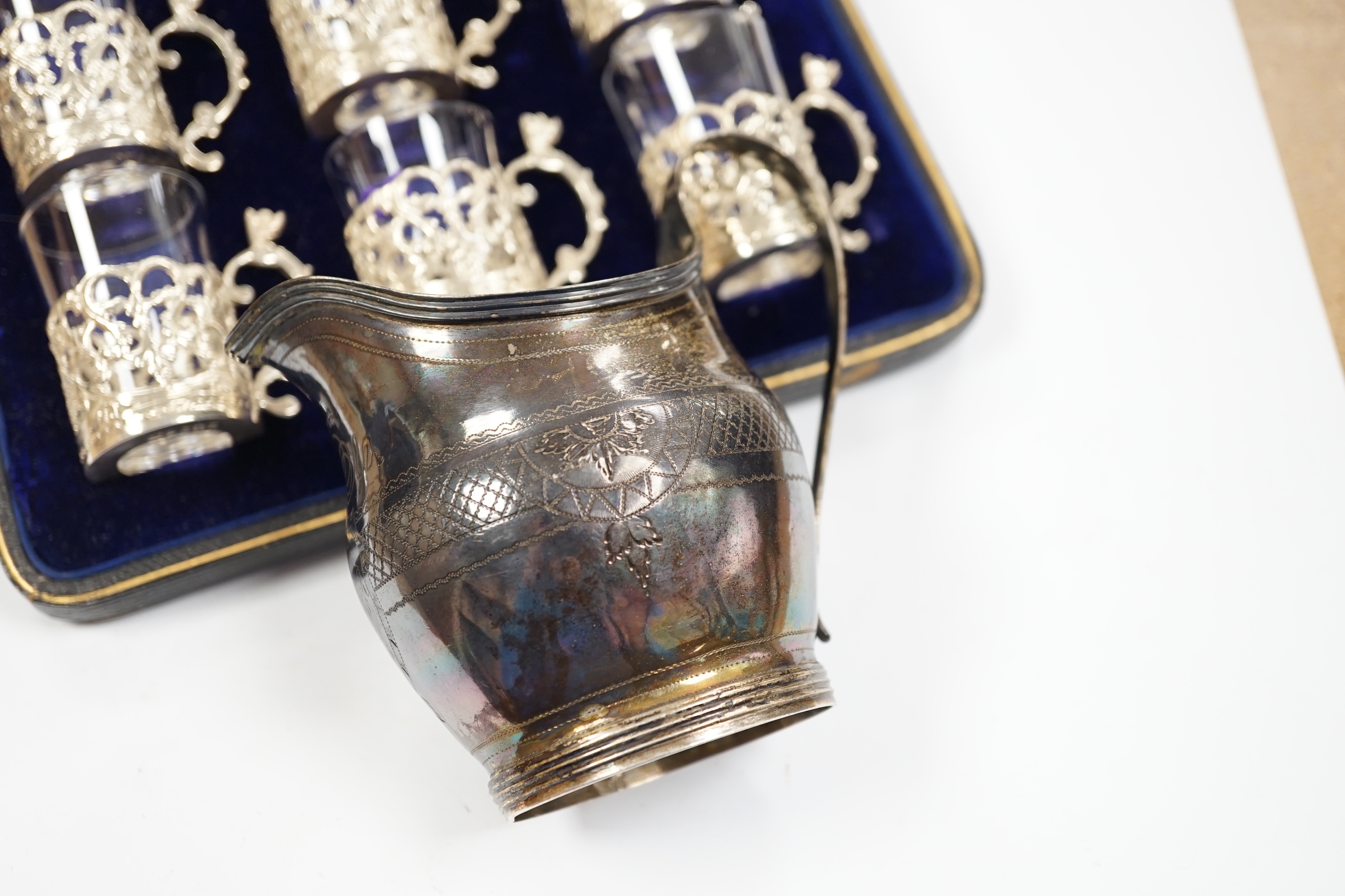 A George III engraved silver helmet shaped cream jug, Francis Purton?, London, circa 1790, height 10.6cm (a.f.), together with a cased set of six George V silver coffee can holders, with glass inserts, Marples & Co, Birm